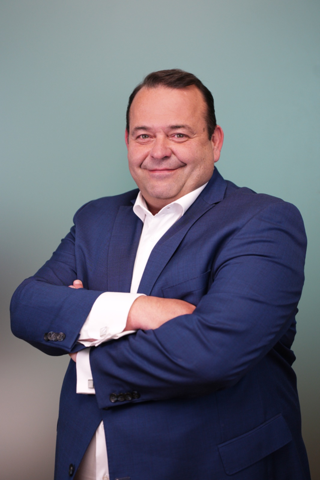 Confident male executive in blue blazer with arms crossed on blue gradient backdrop — corporate headshot by Best Alex Shots, Vienna