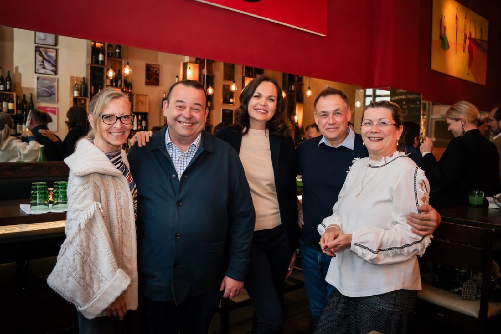 Five smiling guests at a wine bar dinner with red walls, Vienna — event photography by Best Alex Shots